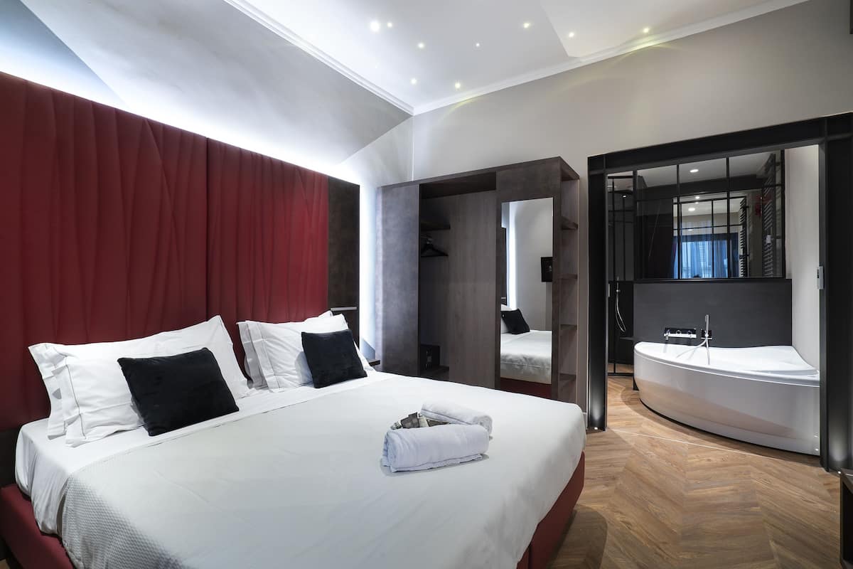 A modern hotel room with a large bed, a red curtain, a built-in wardrobe, and a separate bathroom with a bathtub.