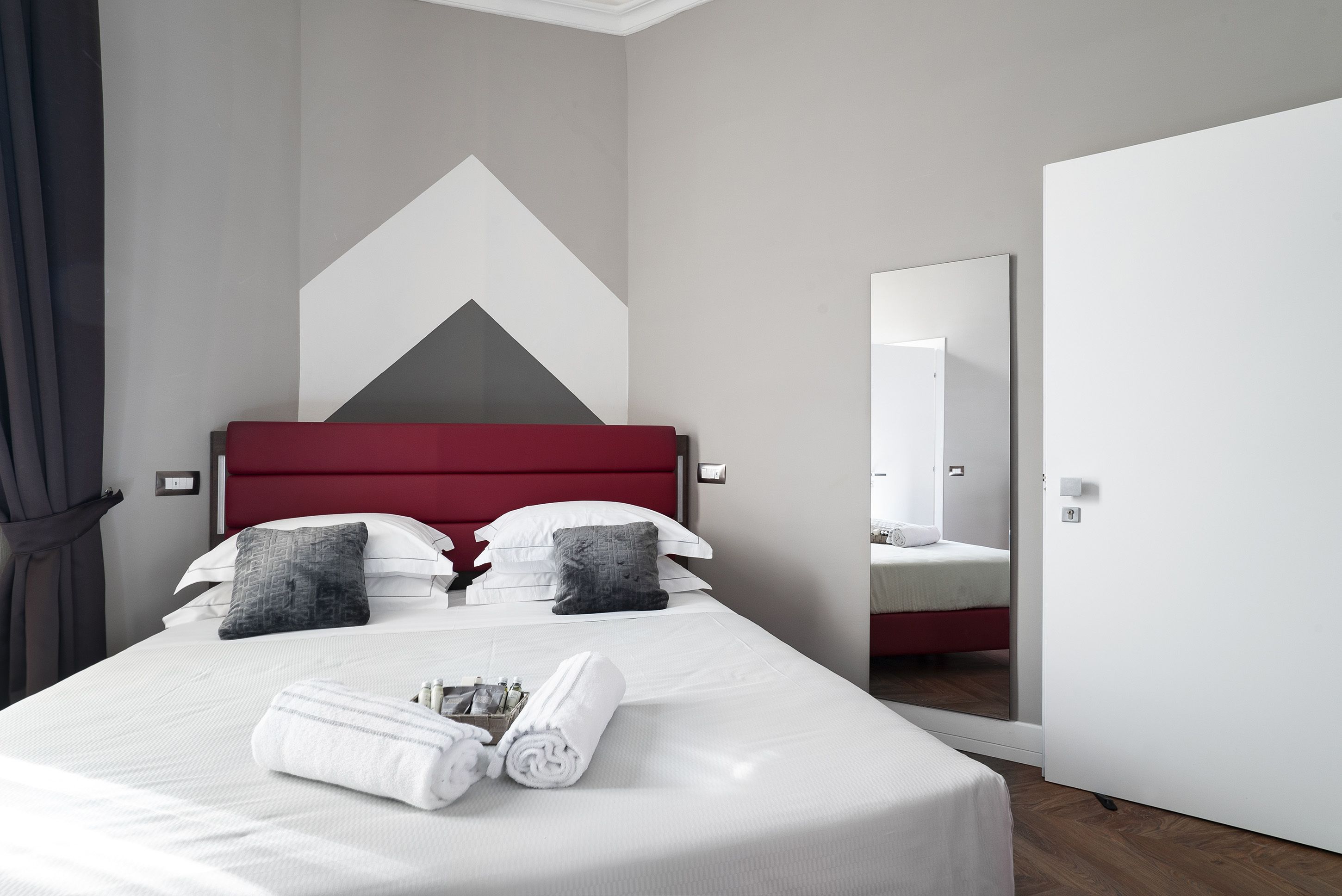 A modern hotel room with a large bed, a red headboard, and a mirror on the wall.