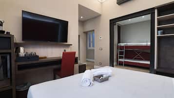 Una camera d'albergo con un letto, una scrivania, una TV, una sedia rossa, un letto a castello e un piccolo balcone.