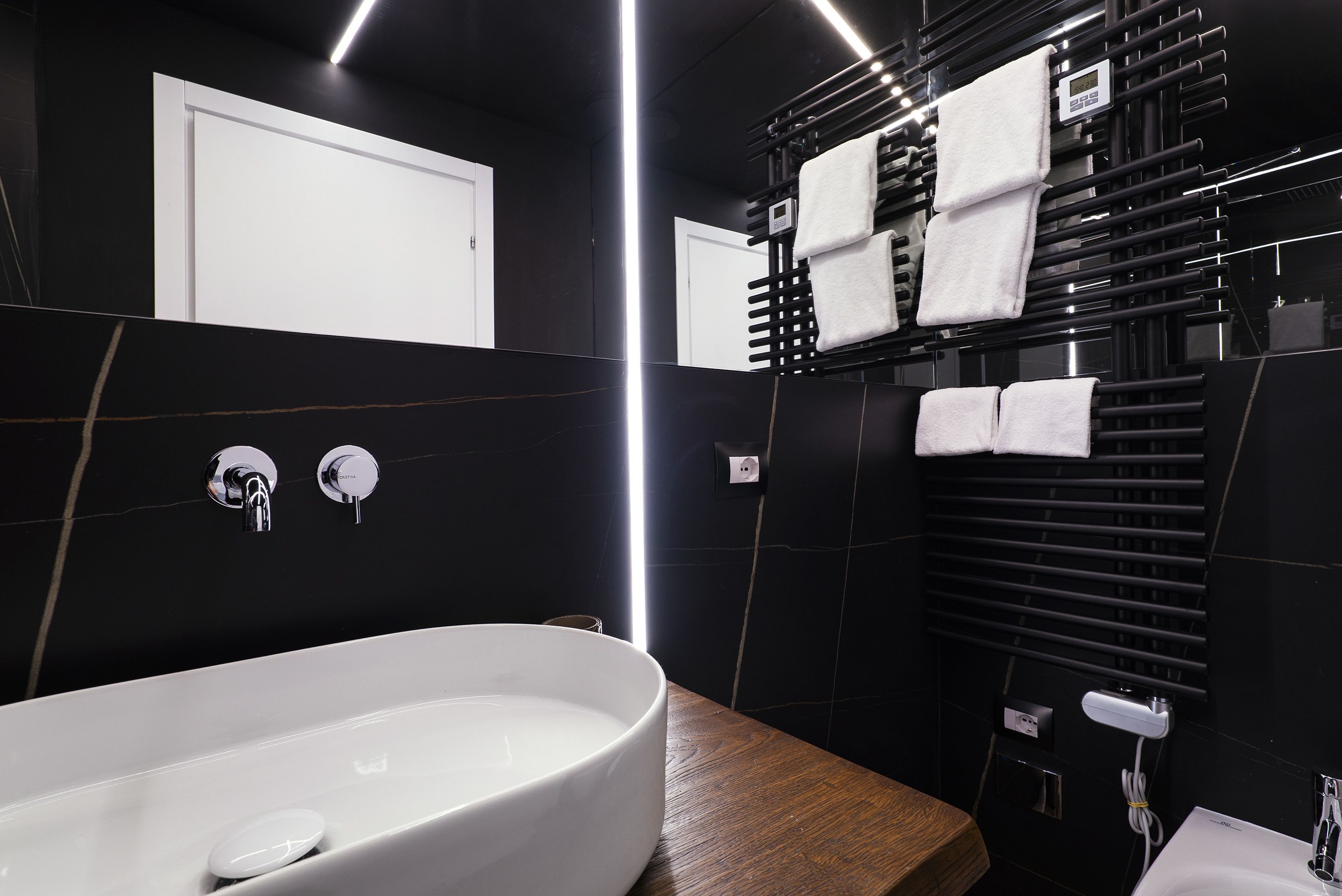 A modern bathroom with a large white sink, black tiled walls, and a wooden vanity.