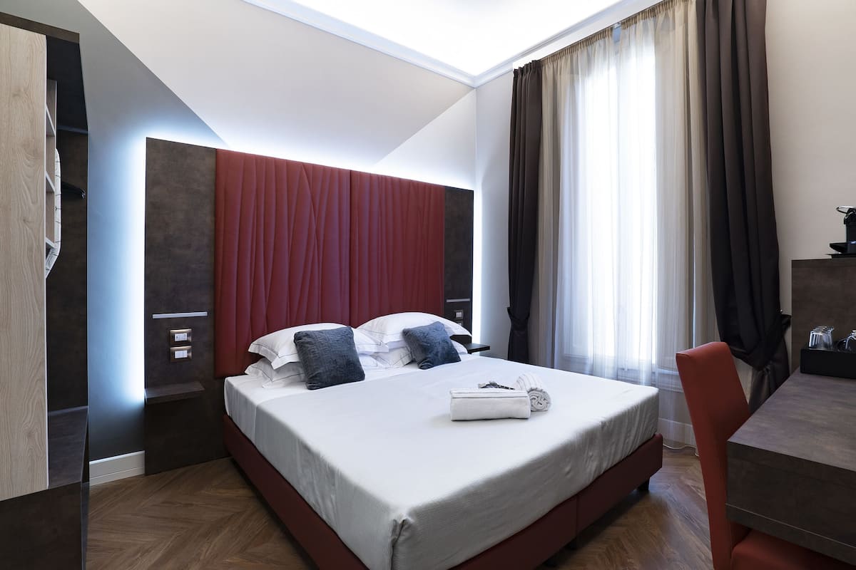 A modern hotel room with a large bed, a desk, and a view of the outdoors.