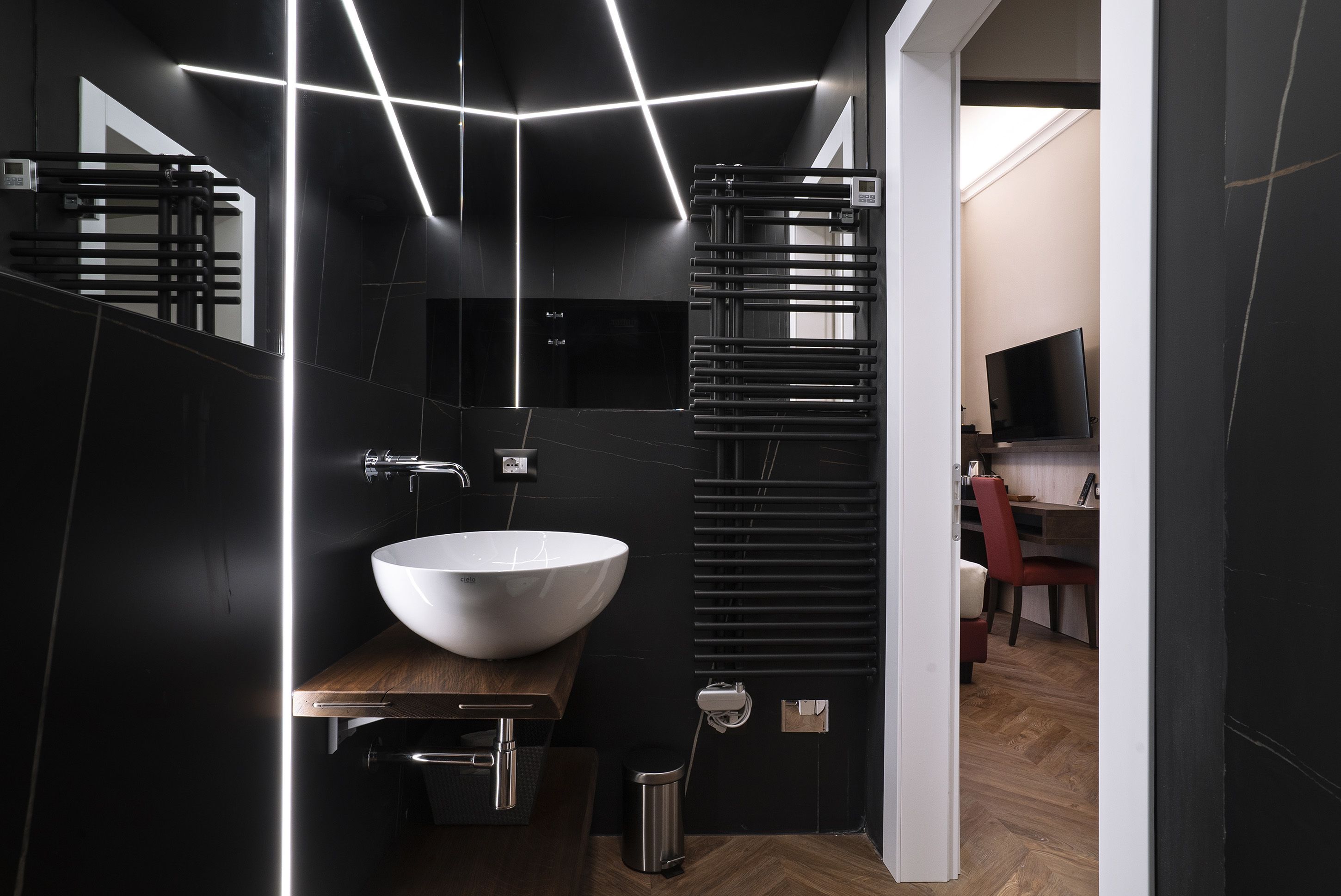 A modern bathroom with a large white sink, dark tiles, and a wooden vanity.
