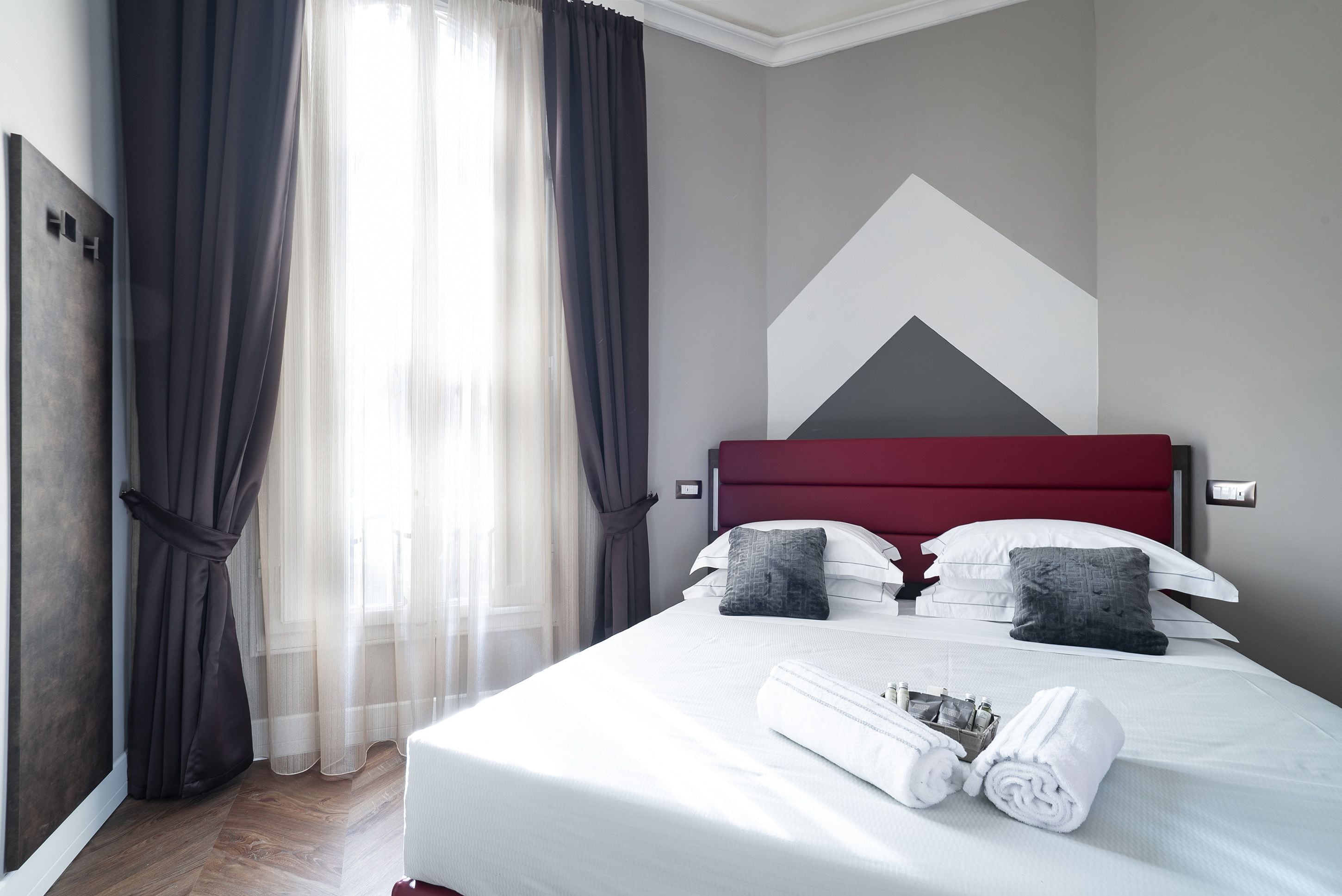 A neatly made bed with white linens, two pillows, and a rolled towel on the side.