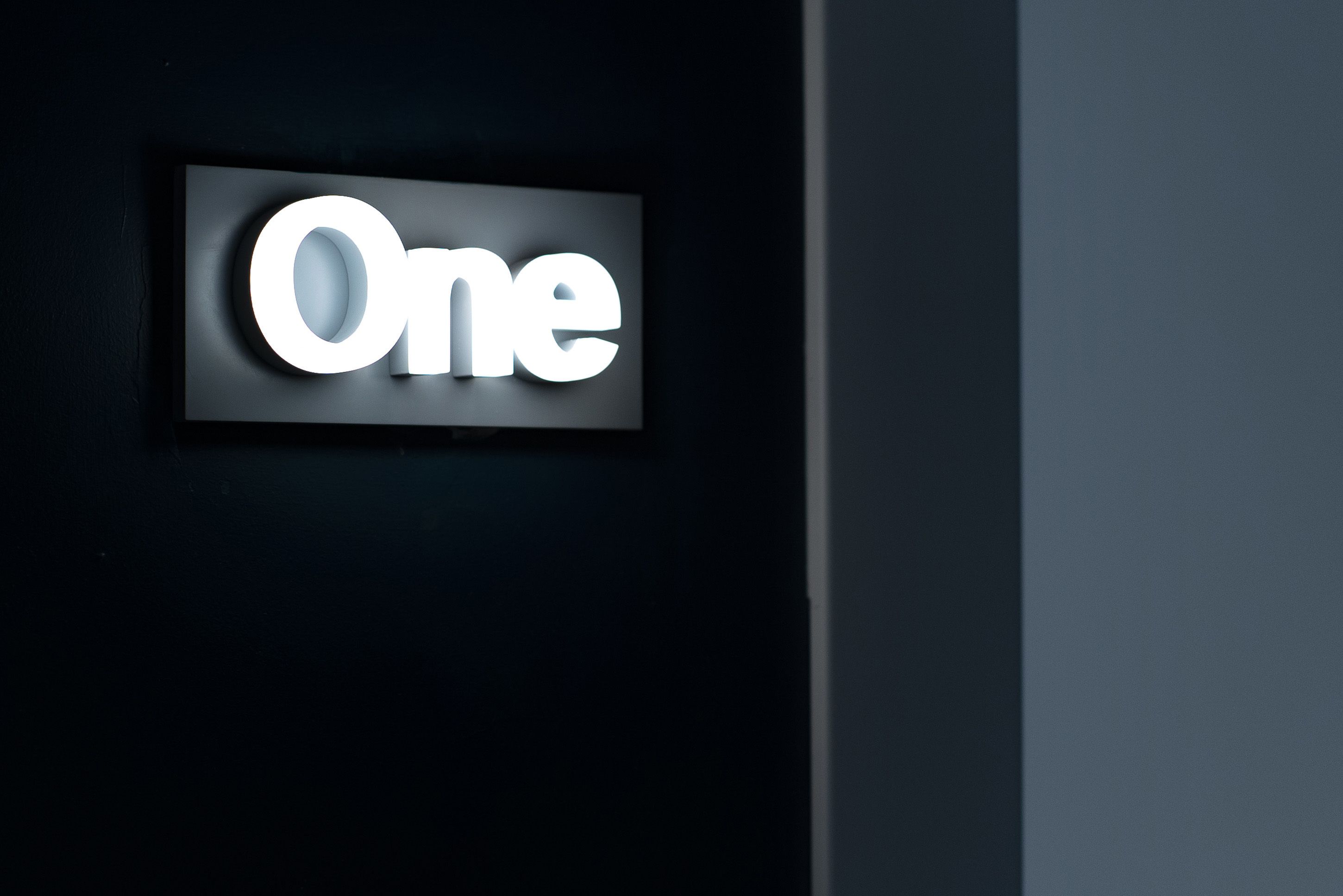 A sign with the word "One" illuminated in white against a dark background.
