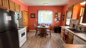 Una cocina con armarios de madera, un refrigerador negro, una estufa y una mesa de comedor con sillas.