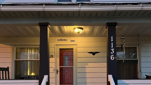 Una casa de dos pisos con un porche delantero, una puerta roja y un letrero que dice 'welcome inn'.