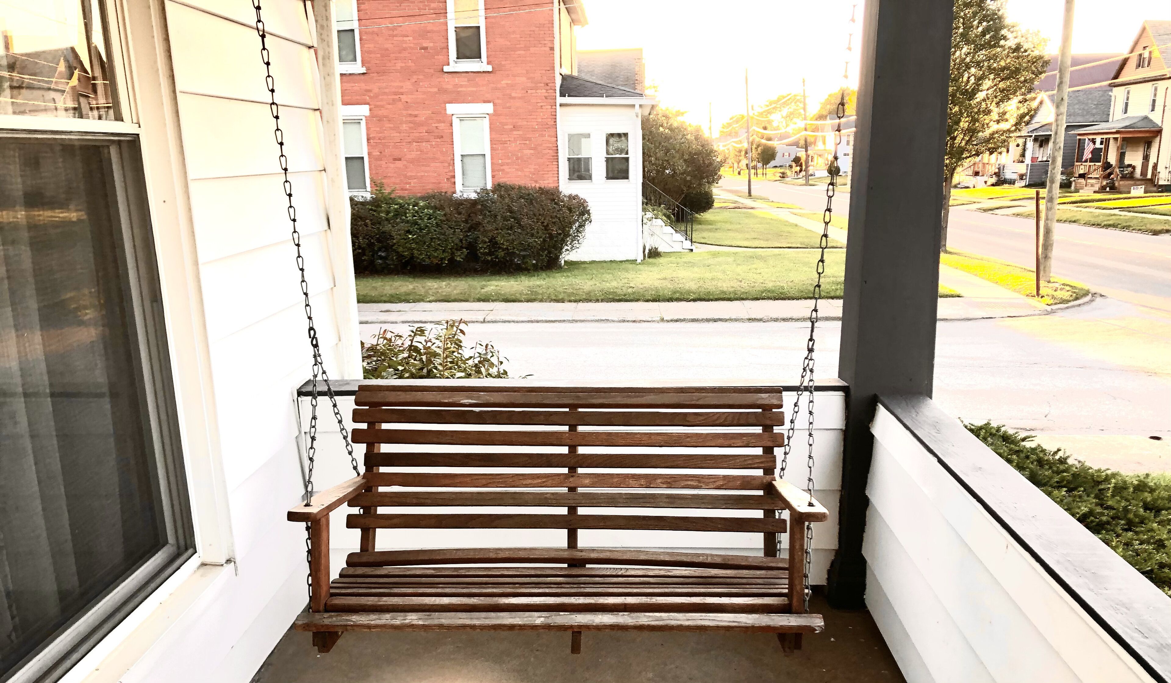 Un banc en bois sur une véranda, avec vue sur une rue résidentielle et des maisons.