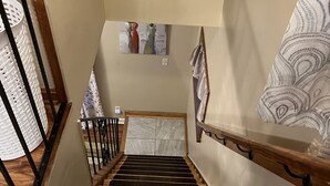 Una escalera de madera con barandilla, un cuadro colgado en la pared y una cortina estampada.