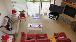 A living room with a beige sofa, red armchairs, a coffee table, a TV, and a fireplace. - 2B Condo w/ Game Tables and Great Views! (Sugar Mountain)