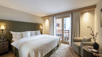 A hotel room with a large bed, a nightstand, a chair, a small table, and a balcony with a view.