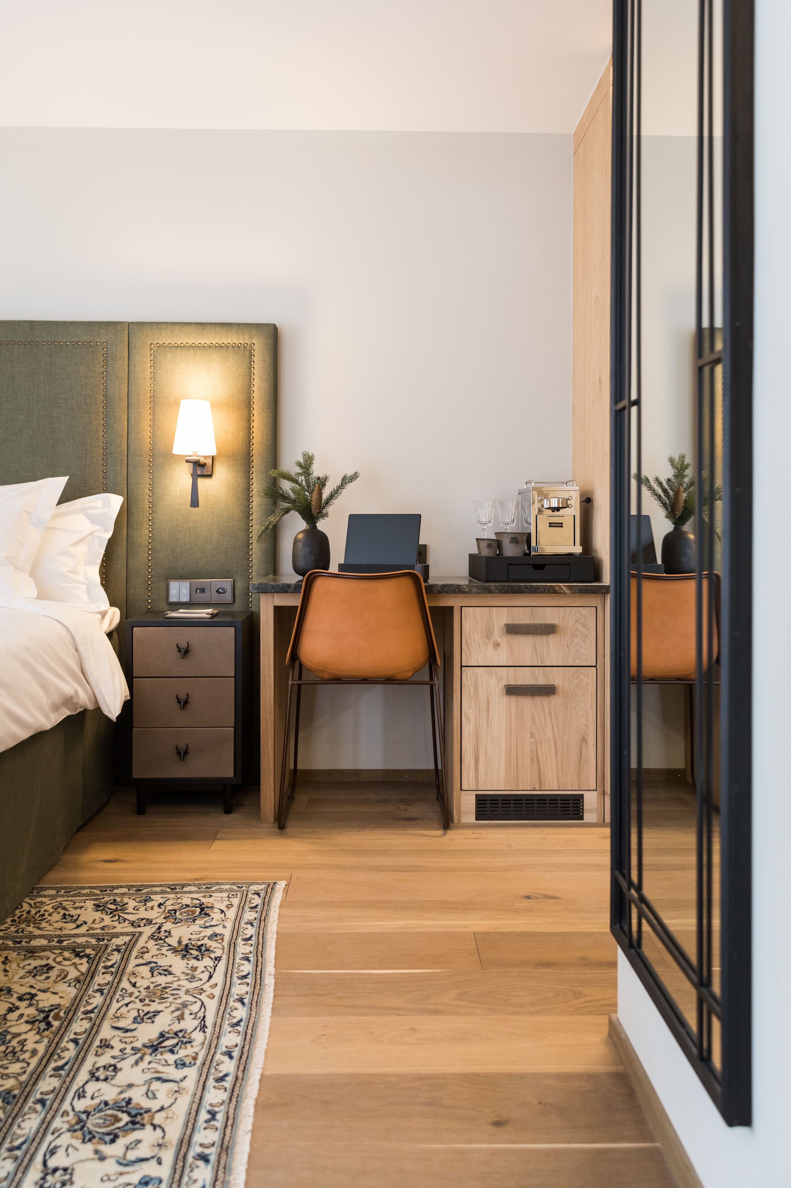 Una camera da letto con un letto, un comodino, una lampada, una scrivania, una sedia e una piccola pianta.