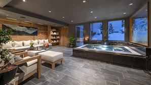 A modern spa area with a hot tub, wooden furniture, and a large window with a snowy view. - Hôtel de Verbier SUP (Bagnes)
