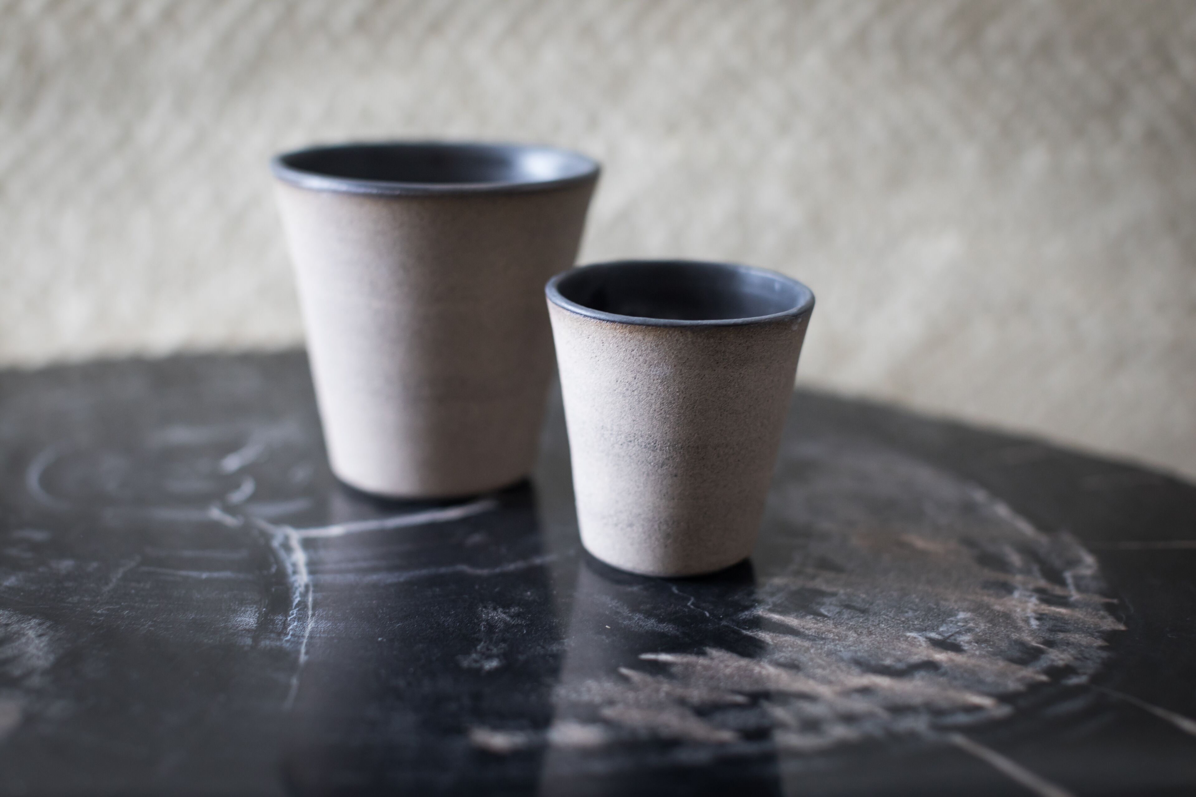 Dos tazas de cerámica sobre una superficie oscura con un fondo texturizado.