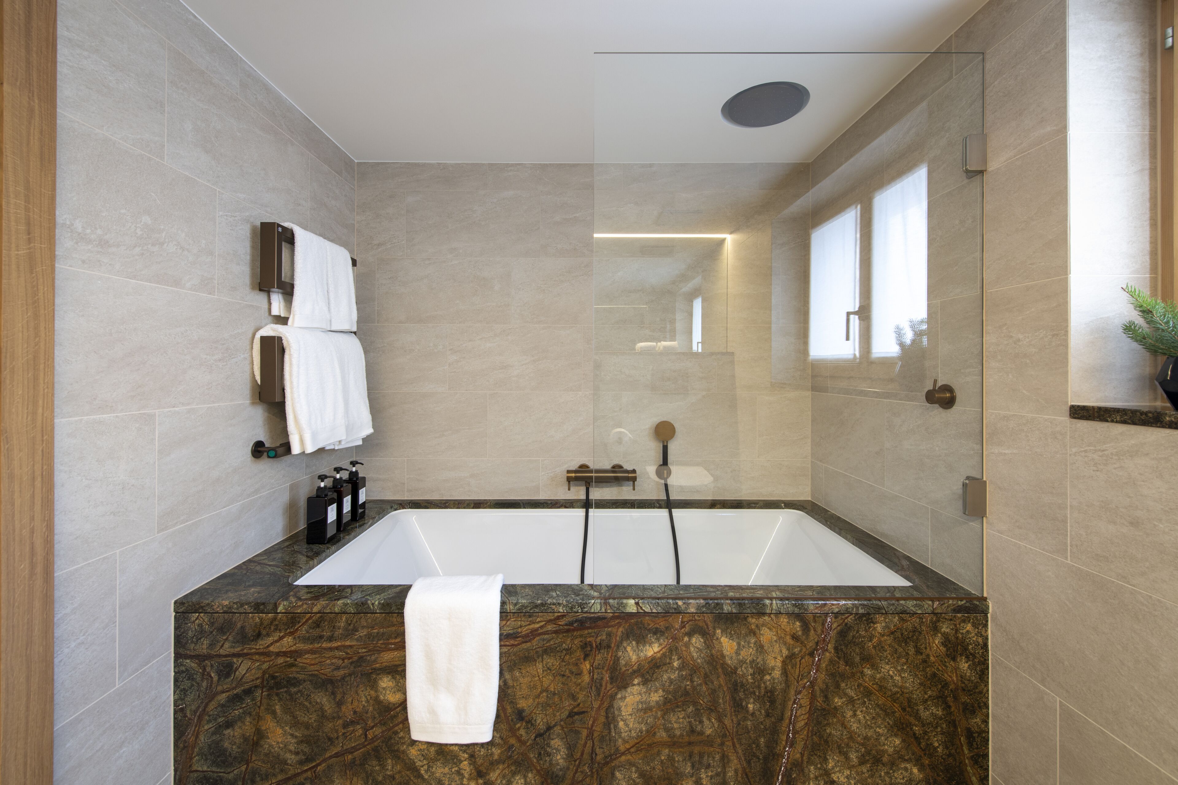 A modern bathroom with a large bathtub, marble countertop, and a glass shower enclosure.