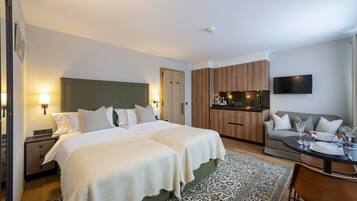 Habitación de hotel con cama doble, sofá, mesa de comedor con sillas, zona de cocina y televisor de pantalla plana montado en la pared.