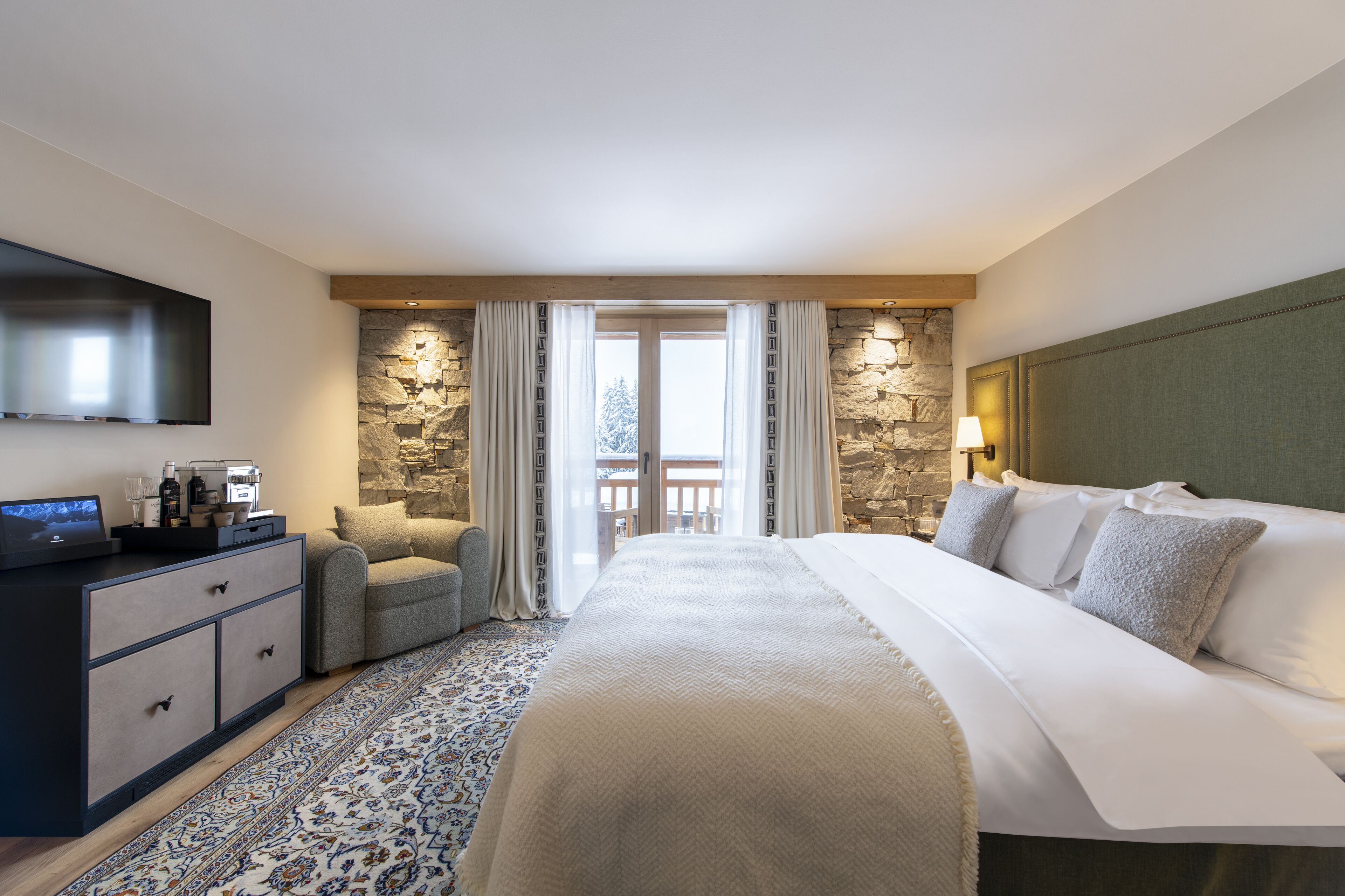 Habitación de hotel con una cama grande, un escritorio con televisor de pantalla plana, una pared de acento de piedra y un balcón con vistas.