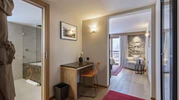 A modern bathroom with a shower, a wooden desk, and a chair. There is a red rug on the floor and a framed picture on the wall.