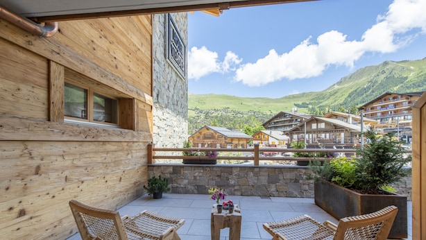 A wooden balcony with wicker chairs and a small table, overlooking a mountain village with traditional buildings. - Hôtel de Verbier SUP (Bagnes)