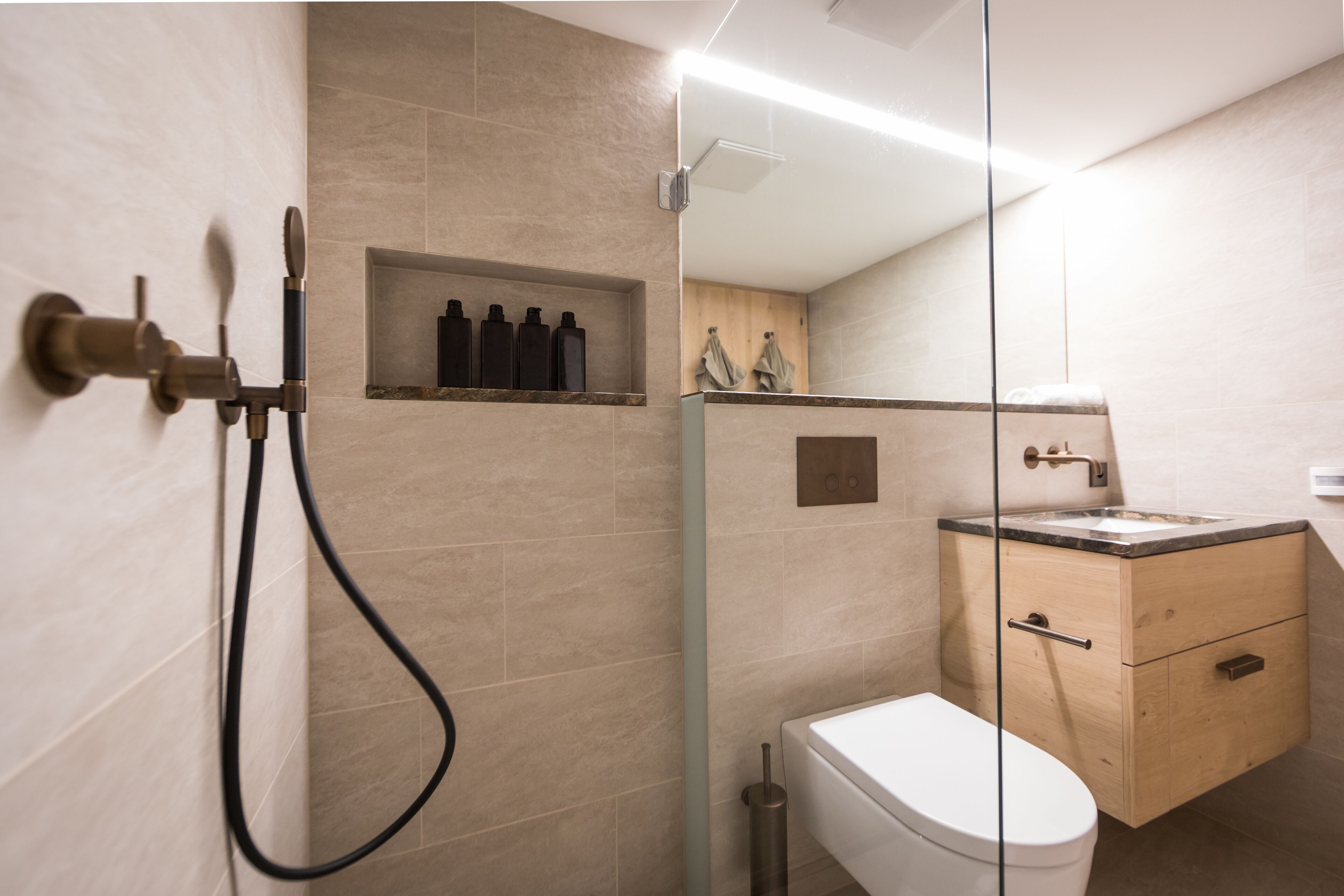 Un baño moderno con ducha envuelta en vidrio, inodoro y tocador de madera con lavamanos.