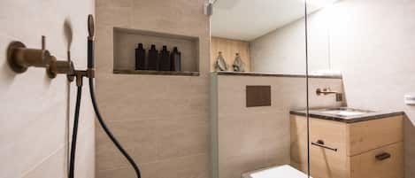 Un baño moderno con ducha envuelta en vidrio, inodoro y tocador de madera con lavamanos.