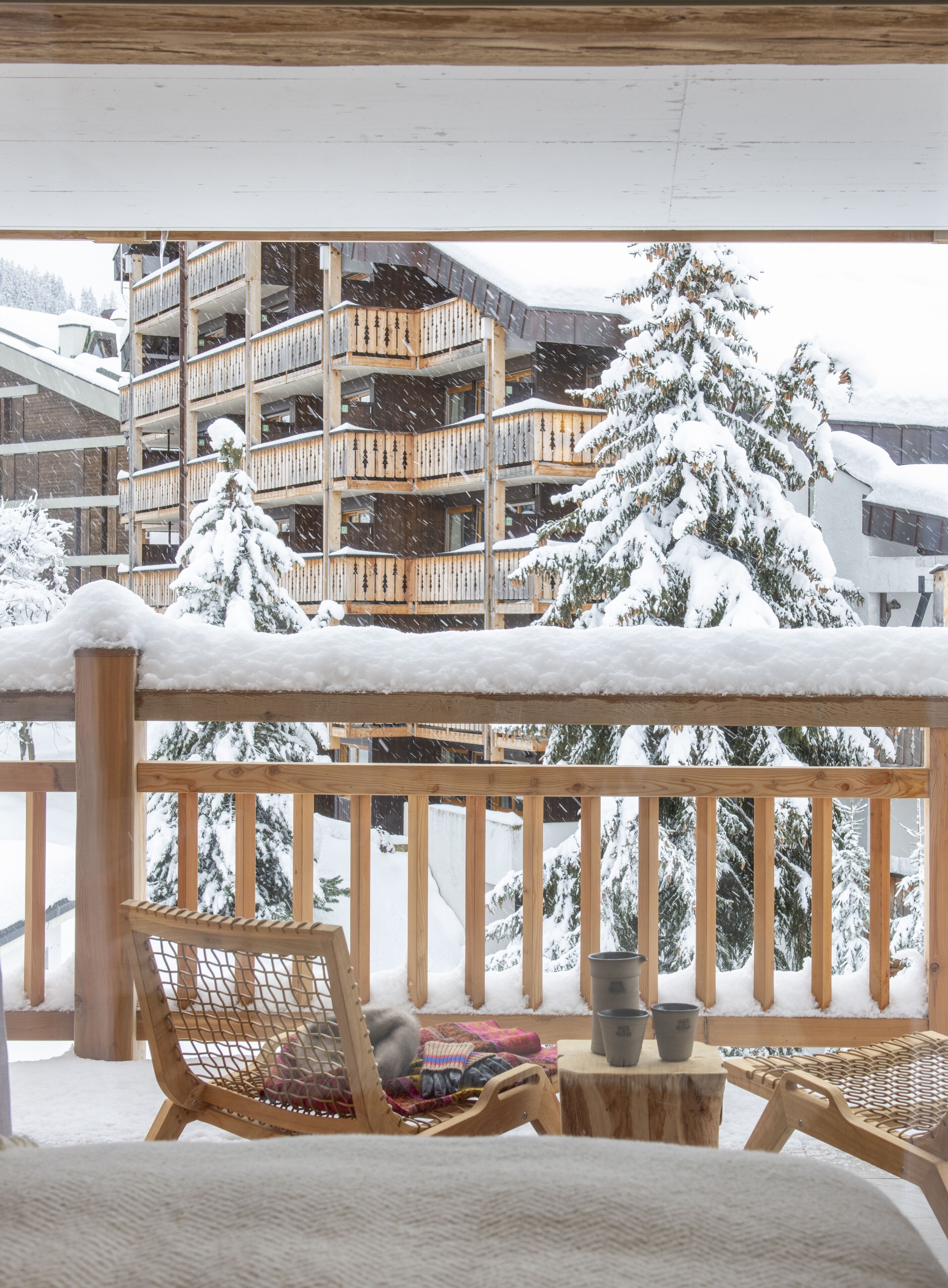 A wooden balcony with a view of a multi-story building and snow-covered trees.