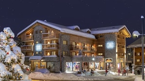 A multi-story hotel with a stone facade, balconies, and a snow-covered roof. - Hôtel de Verbier SUP (Bagnes)