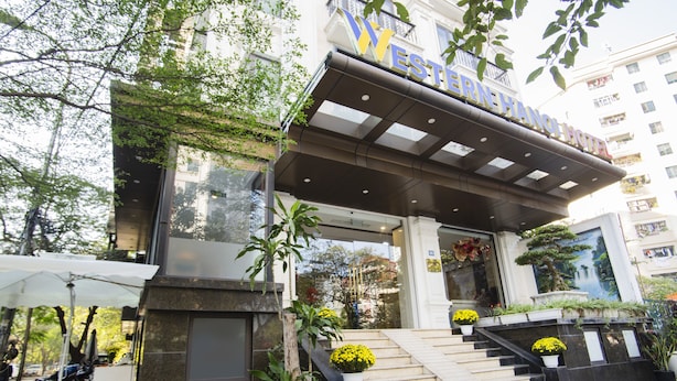 A hotel entrance with a modern design, featuring a prominent sign, a staircase with potted plants, and a covered area with umbrellas. - Western Hanoi Boutique Hotel (Hanoi)