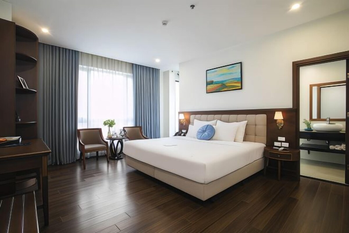 Habitación de hotel con una cama grande, un escritorio, una silla, una mesita con una planta y un cuadro en la pared.