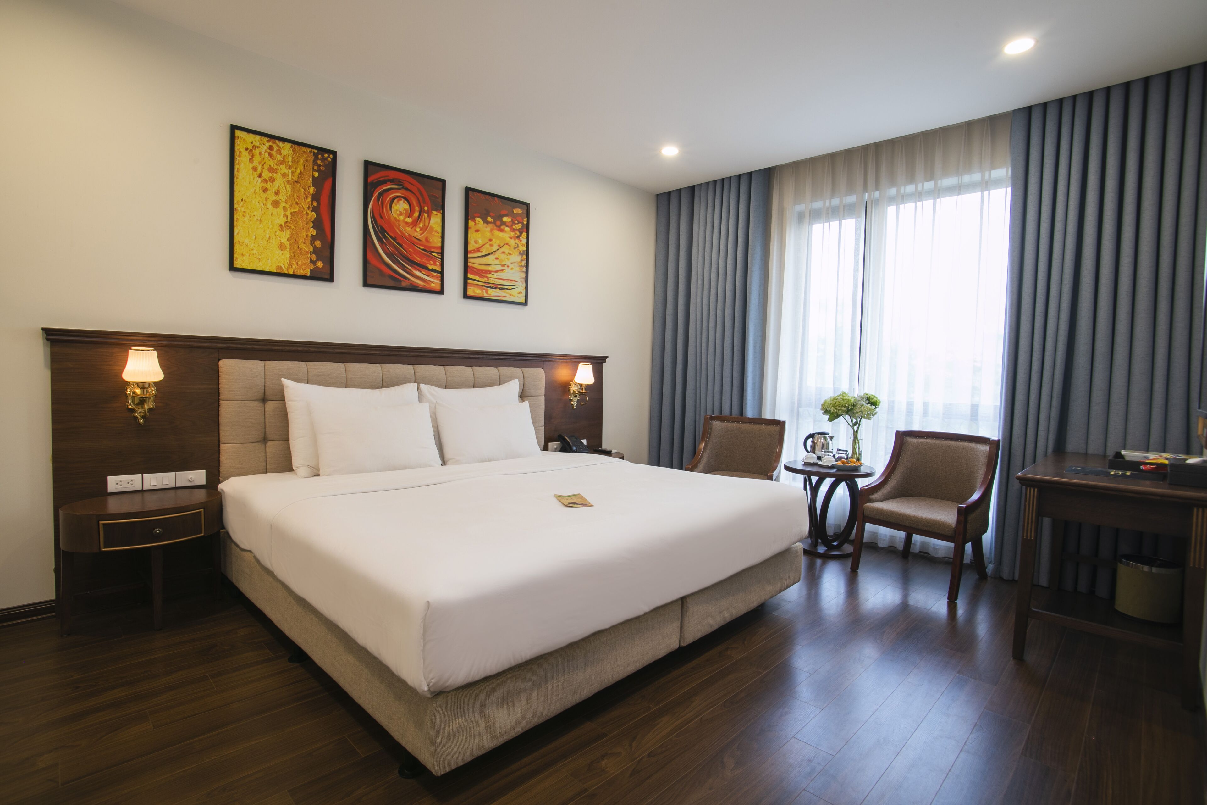 Ein Hotelzimmer mit einem großen Bett, zwei Nachttischlampen, einem kleinen Tisch mit einer Vase und einem Stuhl.