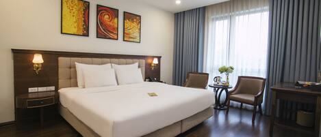 Ein Hotelzimmer mit einem großen Bett, zwei Nachttischlampen, einem kleinen Tisch mit einer Vase und einem Stuhl.