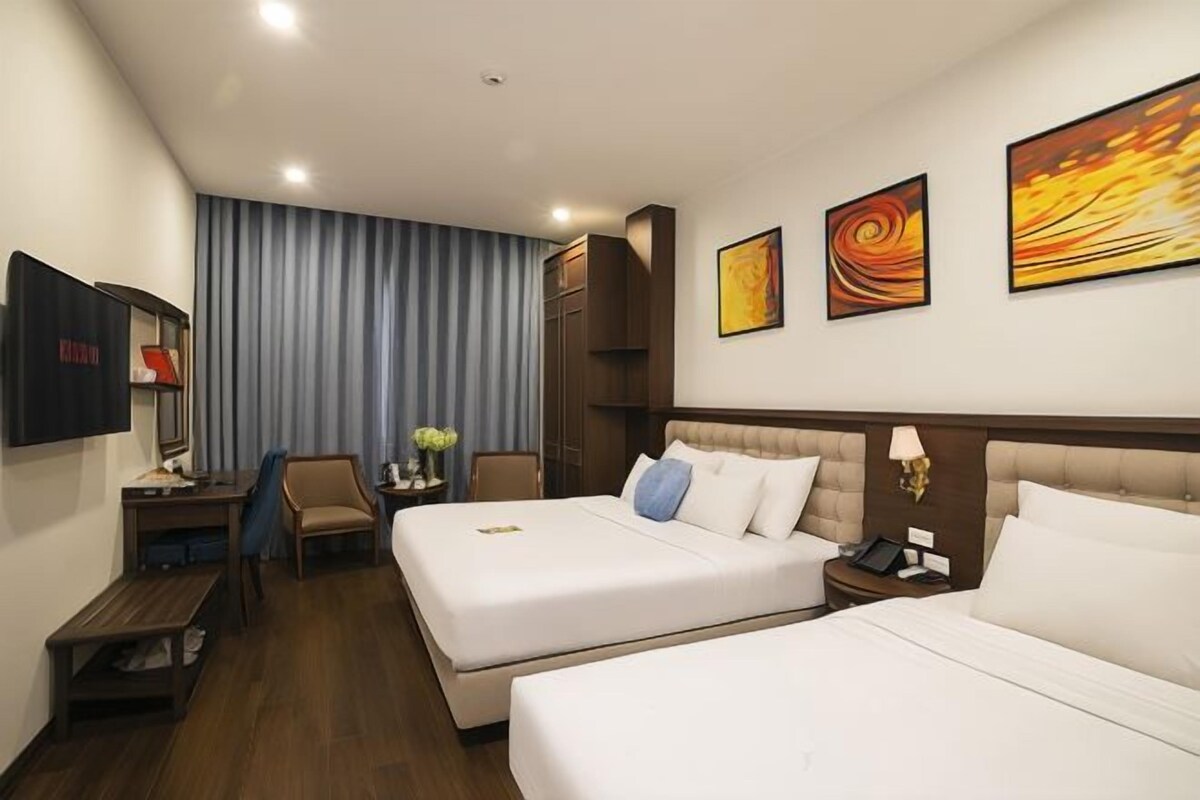 Habitación de hotel con dos camas, un escritorio, una silla, un televisor y obras de arte en la pared.