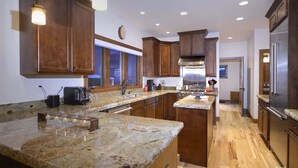 A kitchen with granite countertops, wooden cabinets, stainless steel appliances, and recessed ceiling lighting.