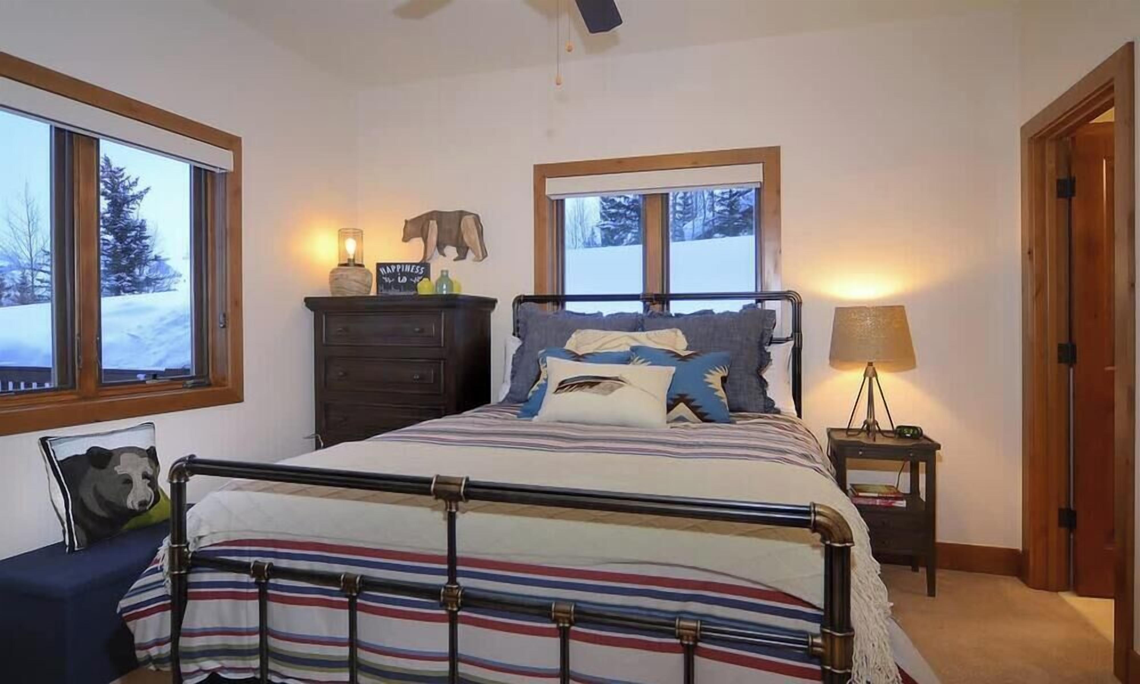 A bedroom with a bed, bedside tables, a dresser, a window with a view of trees, and a door.