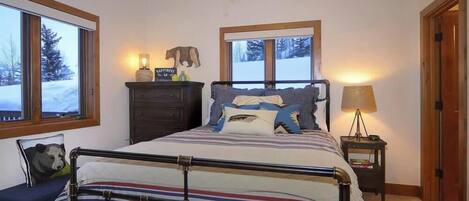 A bedroom with a bed, bedside tables, a dresser, a window with a view of trees, and a door.