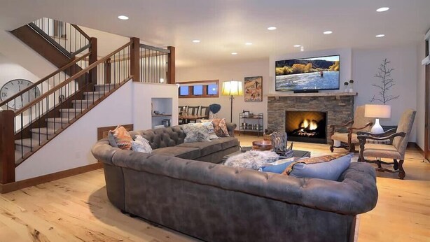 A living room with a sectional sofa, a fireplace, a television, and a staircase.