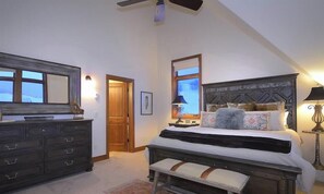 Une chambre à coucher comprenant un lit, une commode, une table de chevet, une lampe et un ventilateur de plafond.