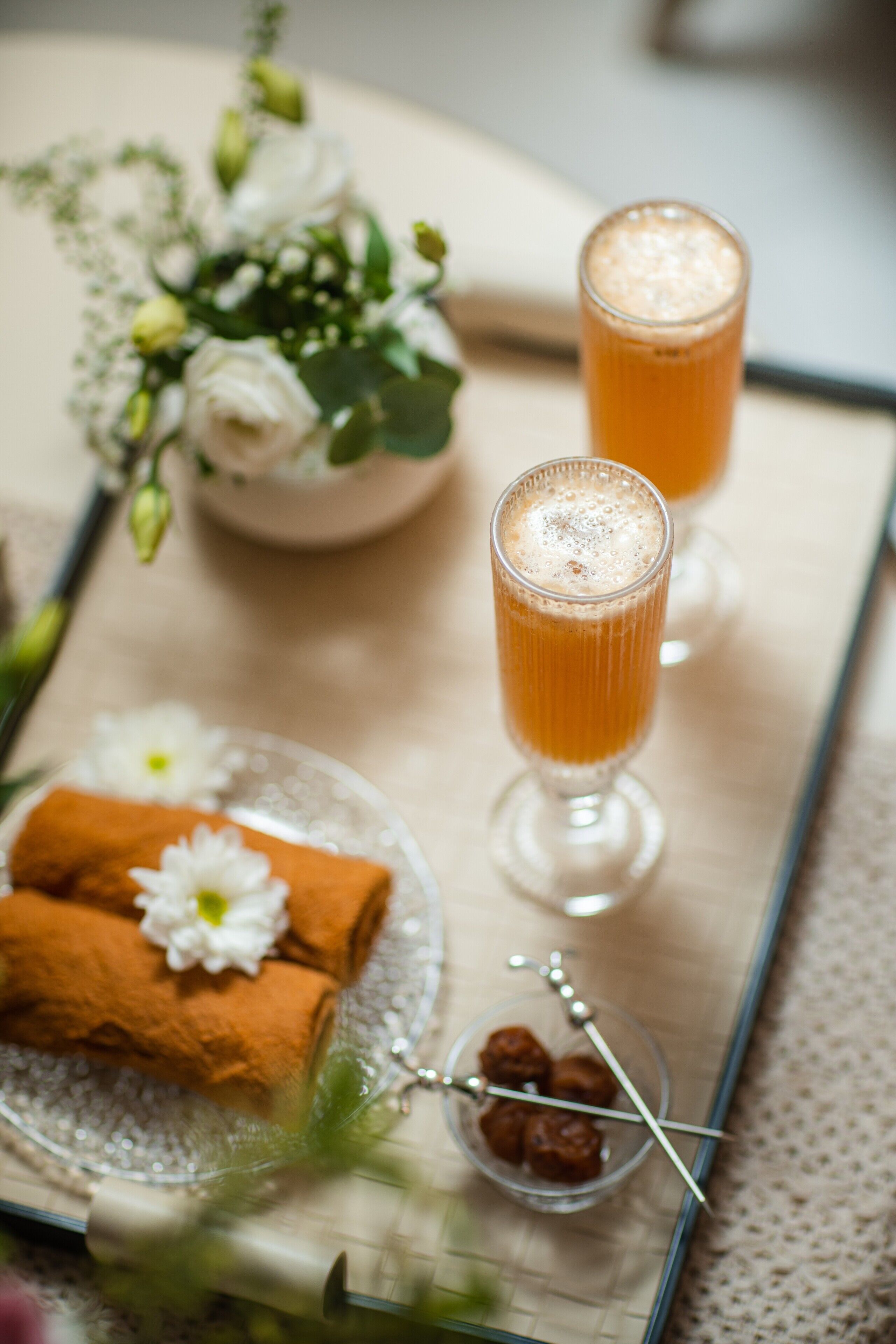 Un plateau avec deux verres de boisson à l’orange, une assiette avec un aliment enroulé et une fleur, et un petit bol contenant des brochettes.