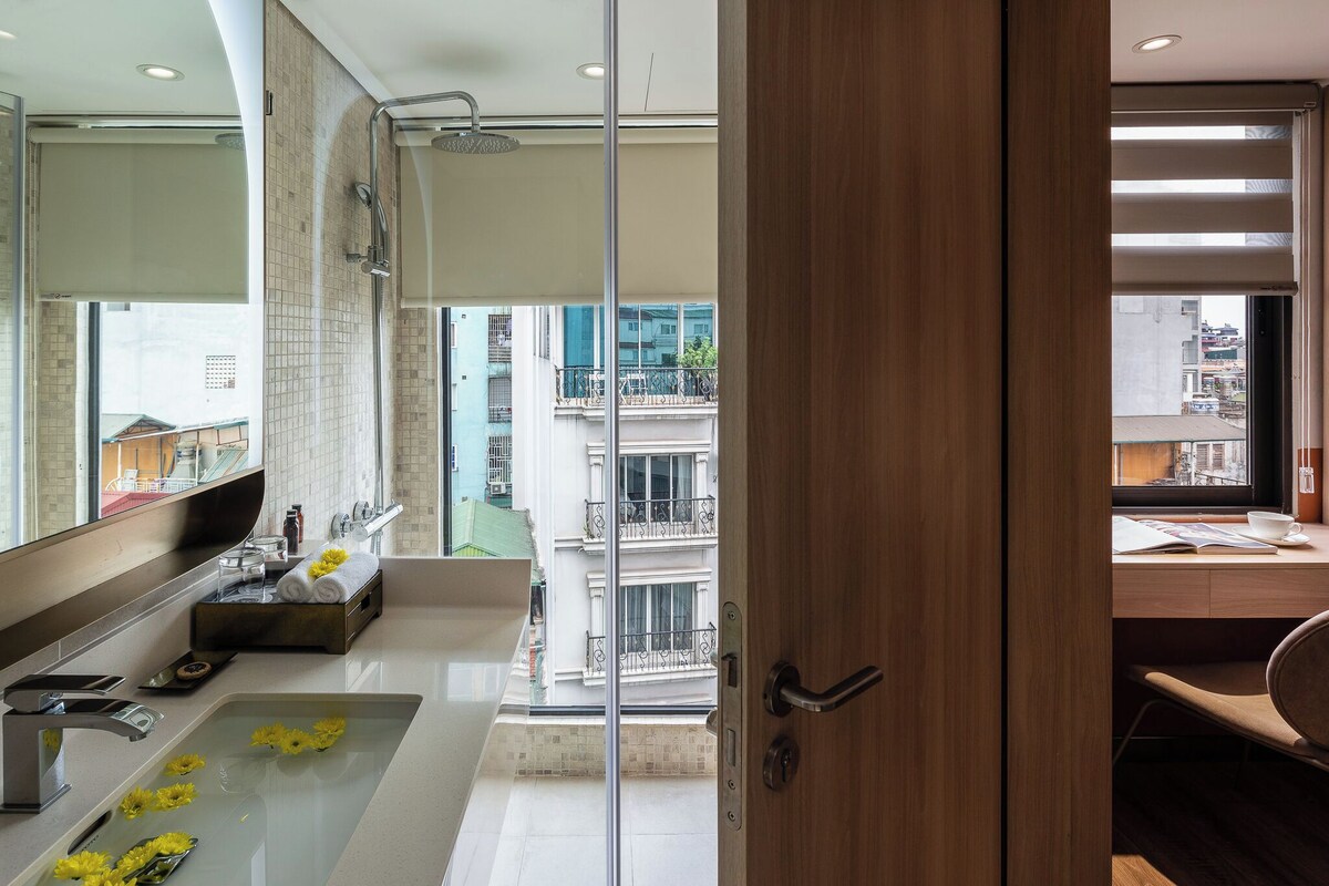 Une salle de bain moderne avec une douche à l’italienne en verre, un grand miroir et une vue sur la ville par la fenêtre.