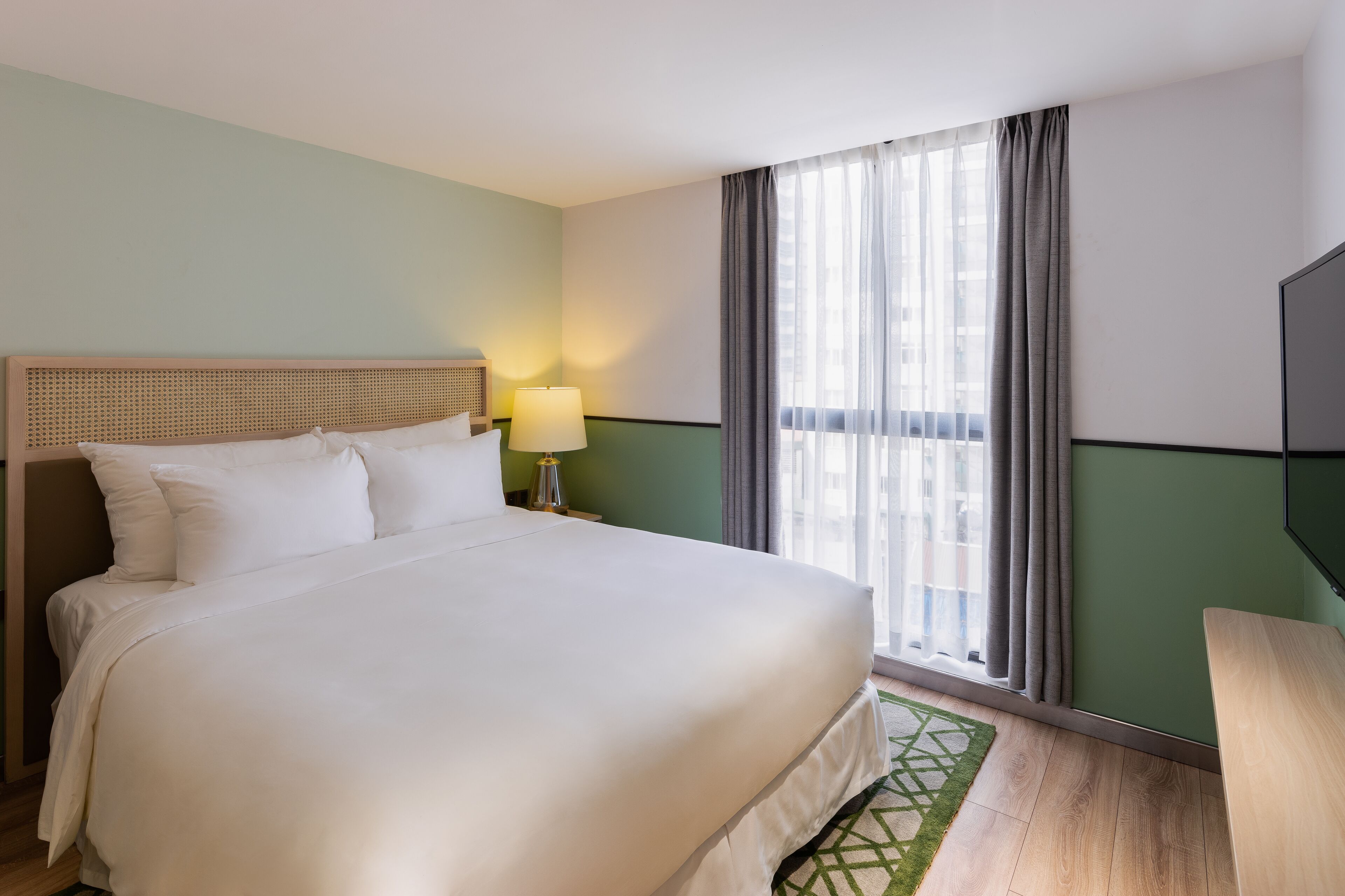 Una habitación de hotel con una cama grande, una lámpara de noche, un televisor y una ventana con cortinas.