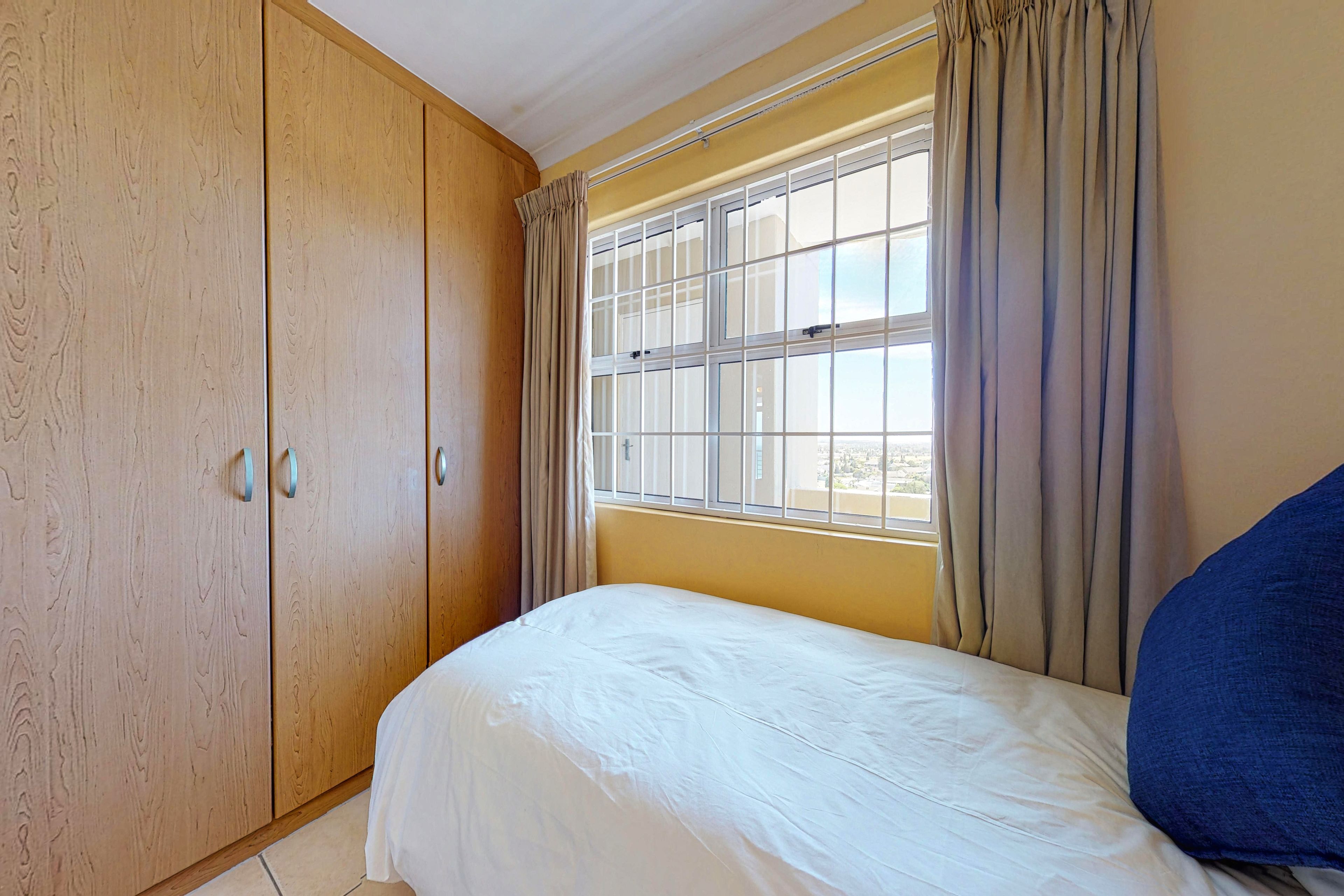 A bedroom with a bed, a wardrobe, and a window with curtains.
