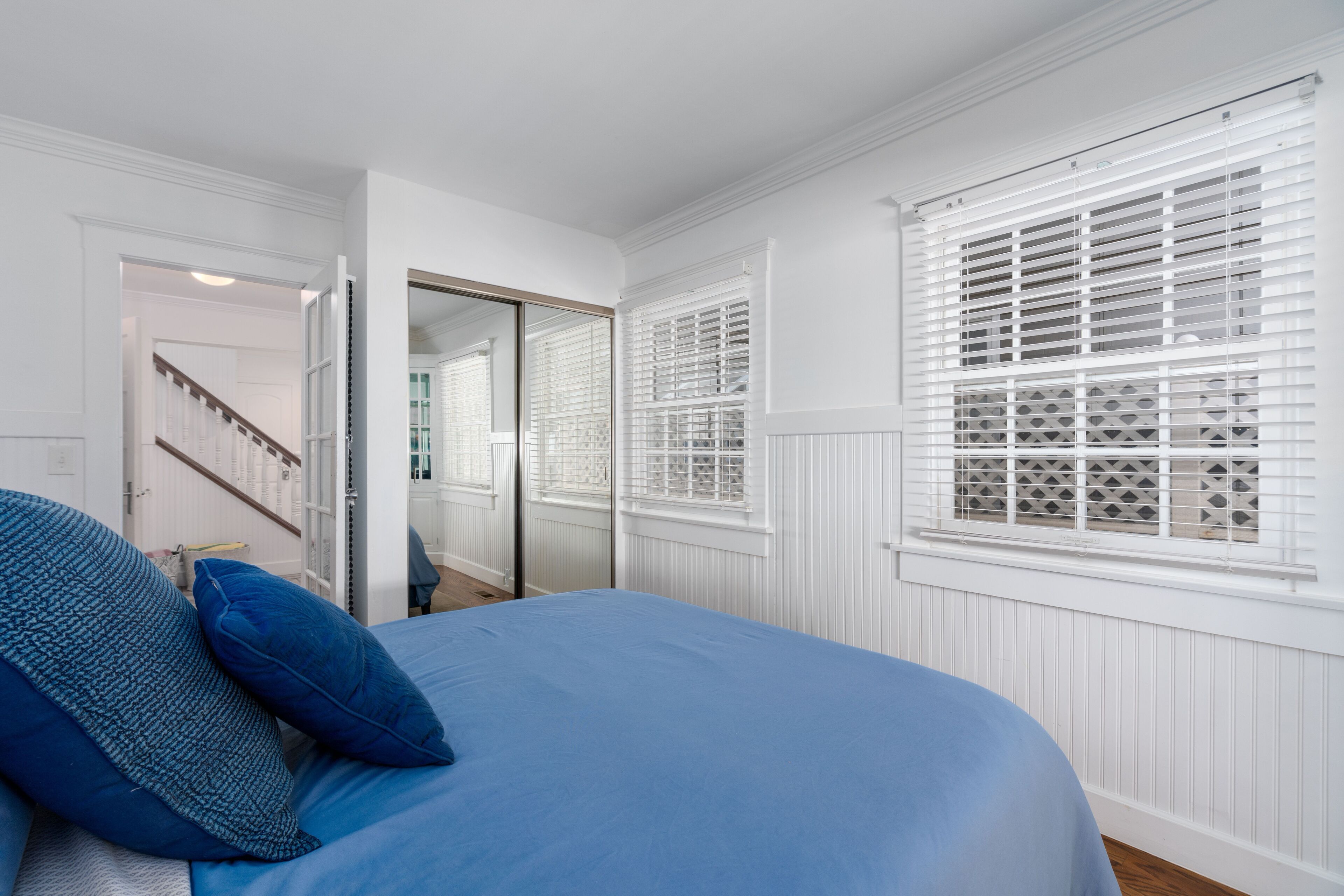 Une chambre à coucher avec un lit, des murs blancs, une fenêtre avec des stores et une porte donnant sur une autre pièce.