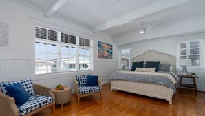 A bedroom with a large bed, two wicker chairs, a small round table, and a painting on the wall.