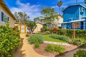 A residential garden with a pathway, various plants, and a blue house.