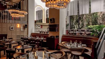 L’intérieur d’un restaurant comprend plusieurs espaces de restauration, notamment des banquettes et des tables, et offre une vue sur un jardin grâce à une grande fenêtre.