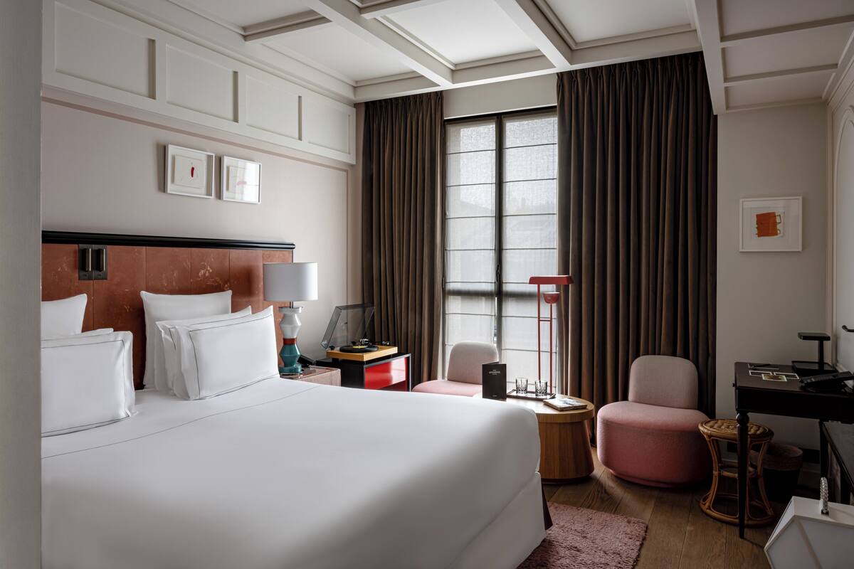 Habitación de hotel con una cama grande, un escritorio, una silla, una mesita y una ventana con cortinas.