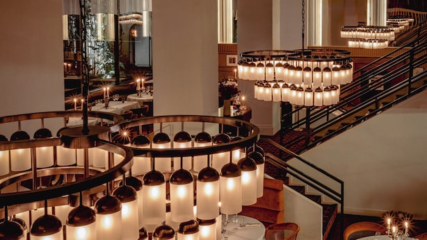 A restaurant with multiple dining tables, a staircase, and a chandelier. - Experimental Marais (Paris)