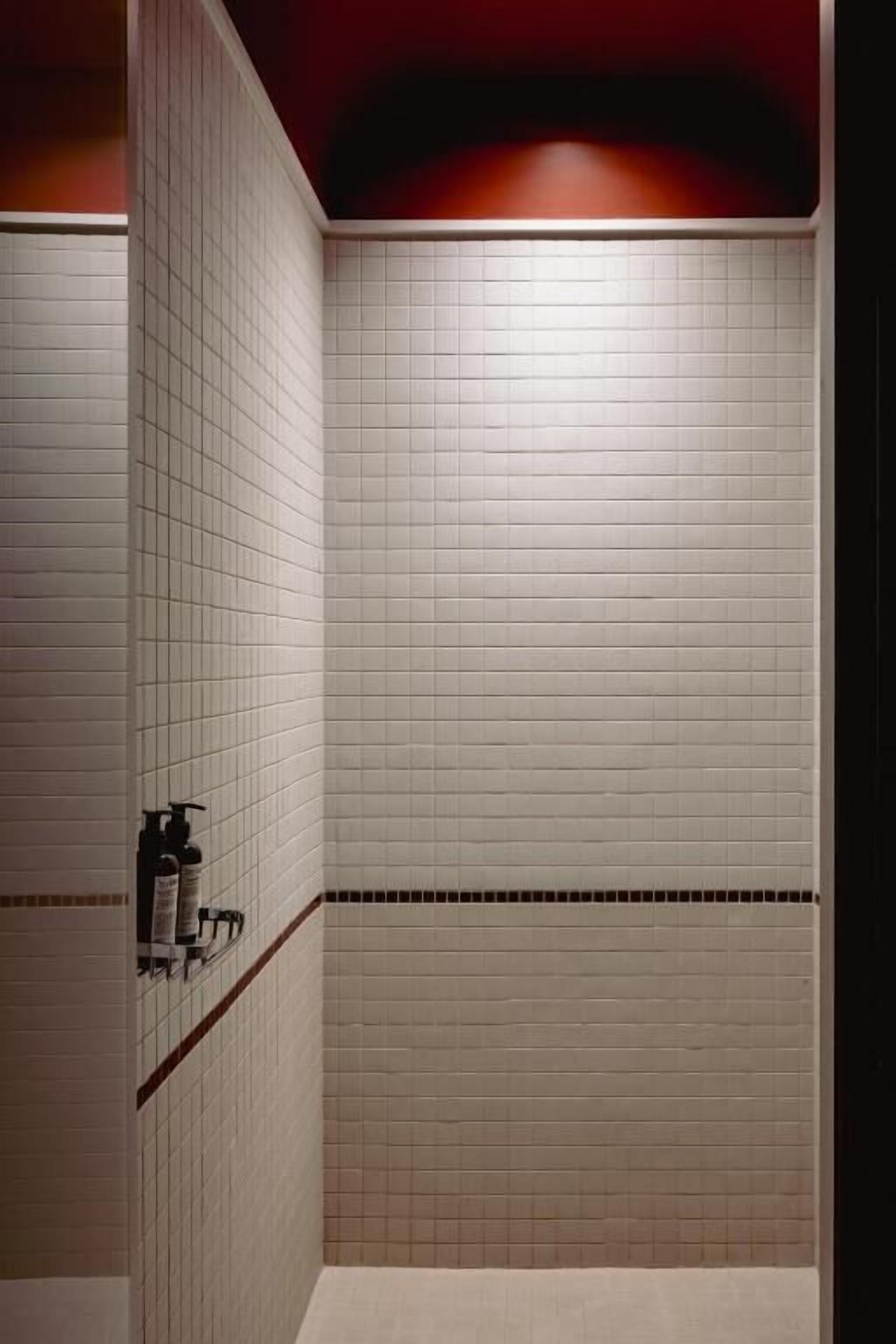 Een betegelde douche met een rode accentmuur en een plank met toiletartikelen.
