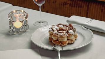 A dessert plate with a pastry on a white tablecloth, a wine glass, and a candle in a glass holder.