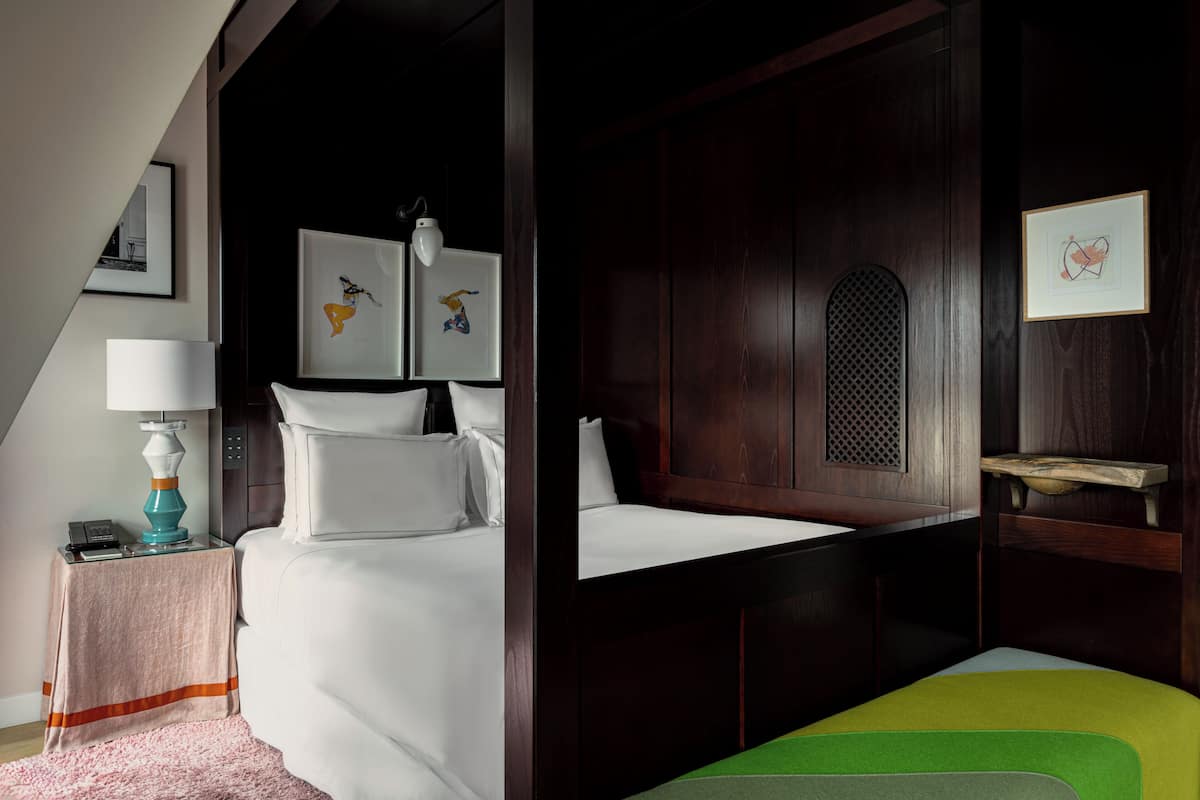 Una habitación de hotel con una cama, una mesita de noche, una lámpara y obras de arte en las paredes.