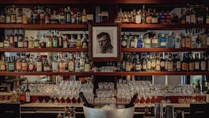 A bar with multiple shelves of liquor bottles and a large bowl of ice with bottles in the foreground. - Experimental Marais (Paris)